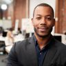 Portrait Of Businessman In Modern Open Plan Office With Business Team Working In Background